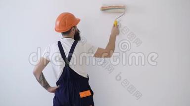 戴安全帽的工人在粉刷墙壁。画家用油漆辊粉刷墙壁的后视图。壁画概念